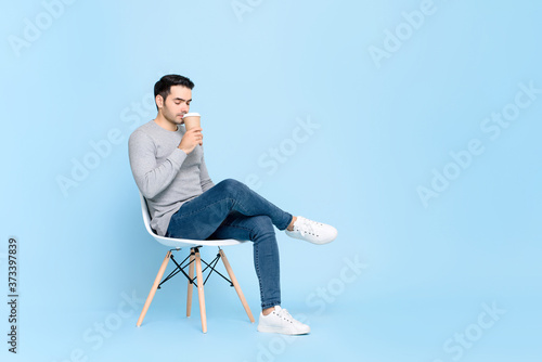 Portrait of young handsome Caucasian man taking a break sitting calmly sipping coffee in isolated studio blue background