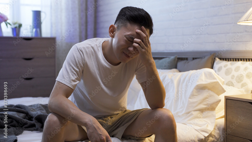 portrait of man sitting at bedside touching forehead is suffering from insomnia. asian male staying awake until daybreak is painful. sleep disorder and health problem concept. portrait of man sitting at bedside touching forehead is suffering from insomnia. asian male staying awake until daybreak is painful. sleep disorder and health problem concept.