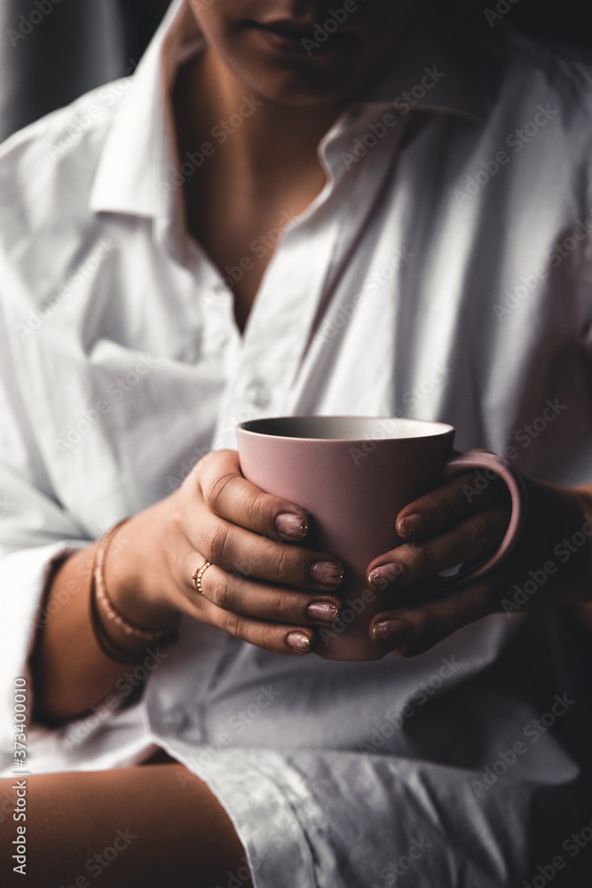 Woman in a white t-shirt holds morning coffee in a pink ceramic cup. Manicure. Front view Woman in a white t-shirt holds morning coffee in a pink ceramic cup. Manicure. Front view