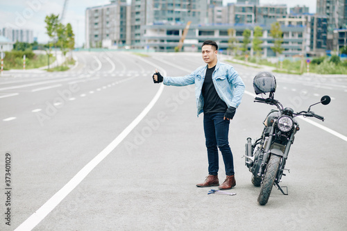 Serious Asian biker catching car on the road as his motorcycle is broken