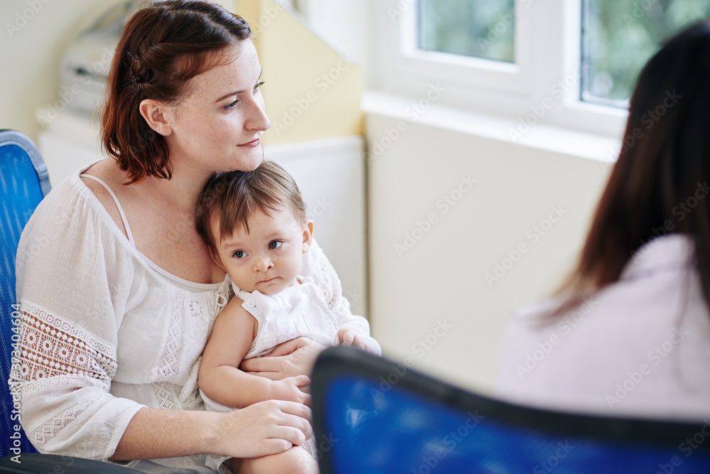Obraz premium Pensive young woman with little daughter on her laps listening to recommendations of pediatrician
