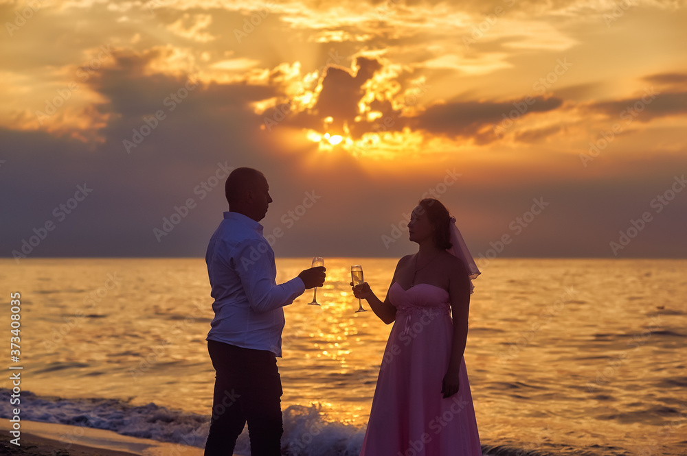A married couple on the sea coast at dawn in wedding dresses in a contoured light