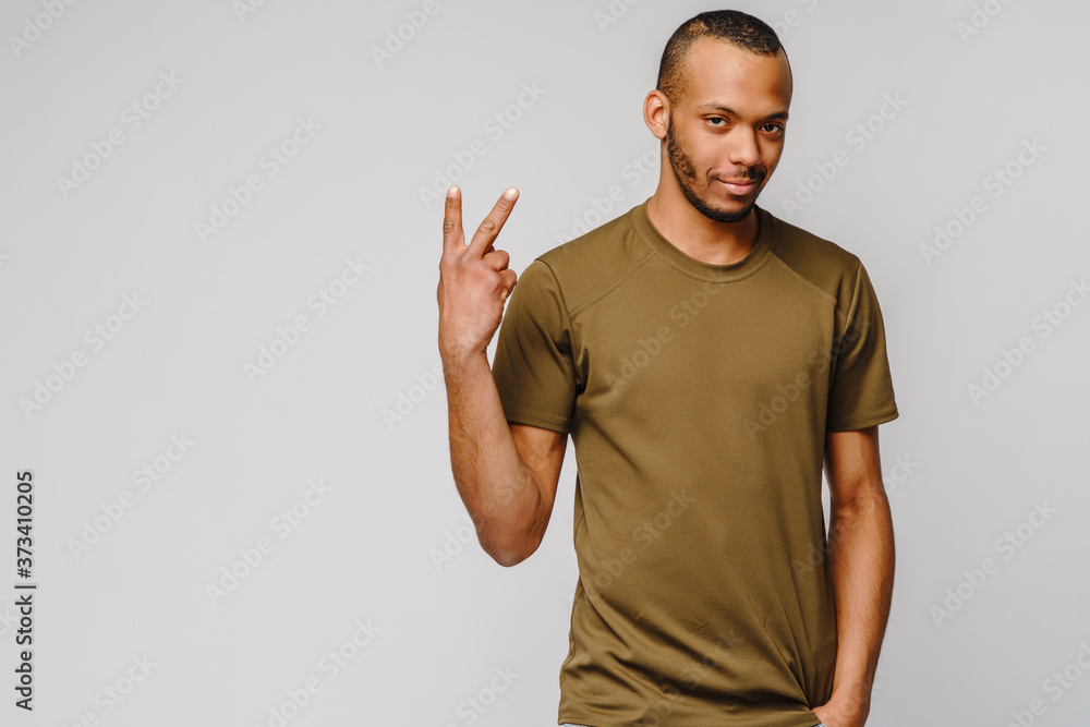 Joyful friendly african-american young man in green t-shirt pointing or showing TWO by finger Joyful friendly african-american young man in green t-shirt pointing or showing TWO by finger