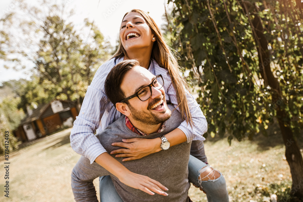 Smiling beautiful young couple in love having fun in park. Handsome man giving piggy back to his girlfriend. Smiling beautiful young couple in love having fun in park. Handsome man giving piggy back to his girlfriend.