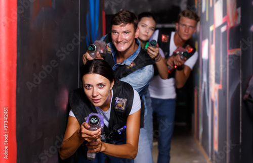 Group glad emotional people with laser guns playing laser tag game together in dark corridor