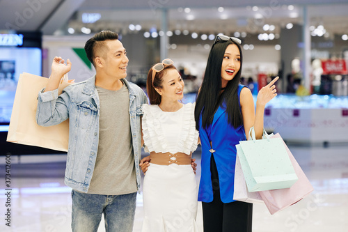 Portrait of cheerful young Asian man and women with shopping bags standing in mall and looking away © DragonImages