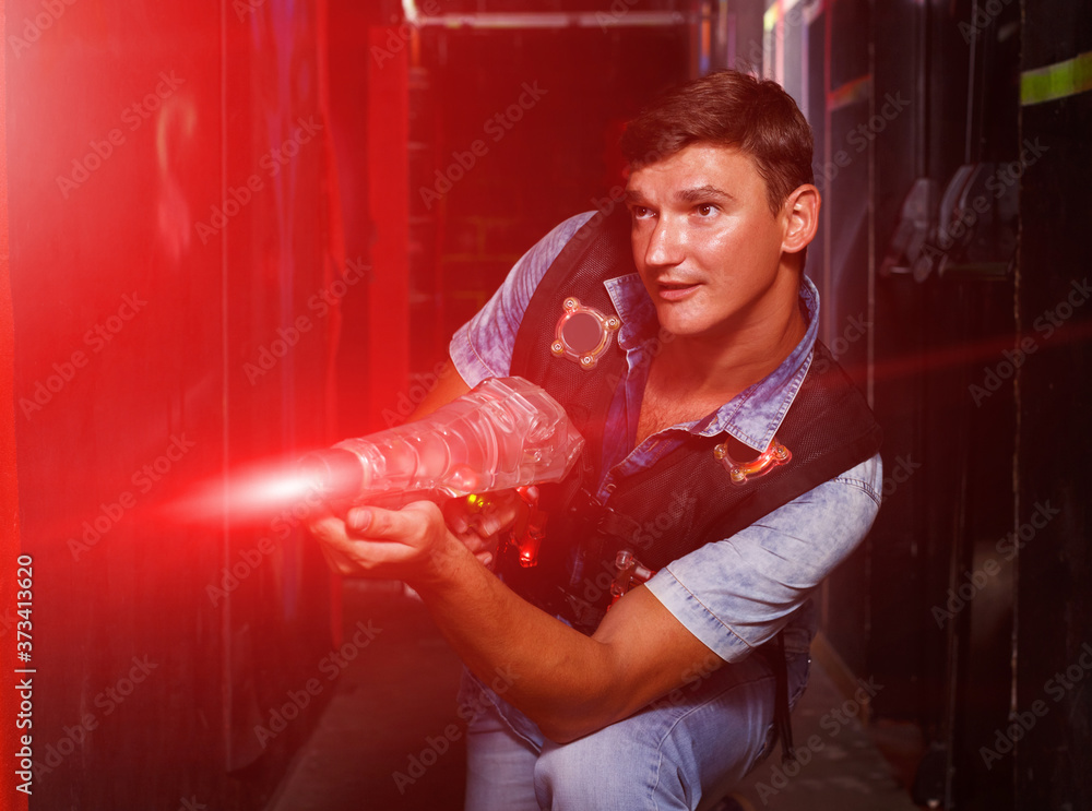 Portrait of positive guy took aim colored laser guns during laser tag game in labyrinth
