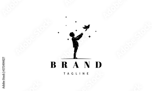 Vector logo on which an abstract image of a silhouette of a boy releasing a bird on the background of stars.
