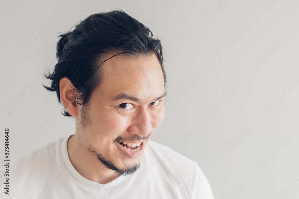 Funny grinning smile face of Asian man in white t-shirt and grey background. Funny grinning smile face of Asian man in white t-shirt and grey background.