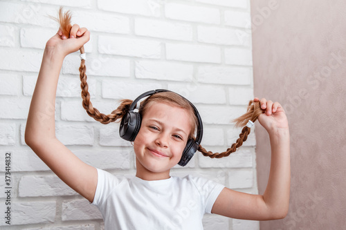 Little girl in big headphones listens to music and laughs smiles