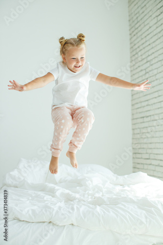 Fototapeta Naklejka Na Ścianę i Meble -  Little girl in bed with white linen. A child at home in the morning wakes up in his room. High quality photo.
