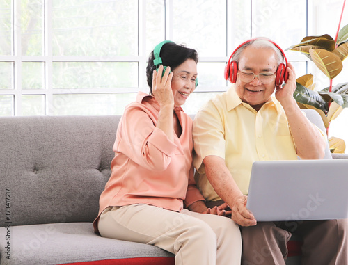 Slika na platnu Asian senior couple having goodtime together , listen to the music from headphones with computer laptop on lap