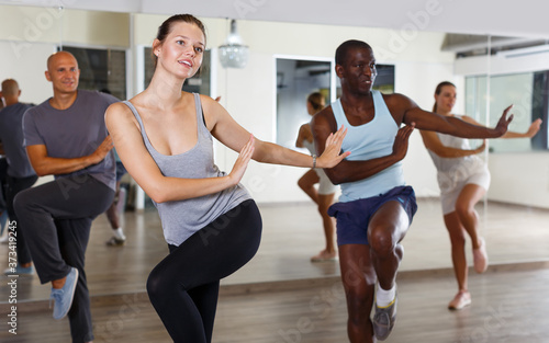 Group of multinational smiling adult people enjoying active dance techniques in modern studio