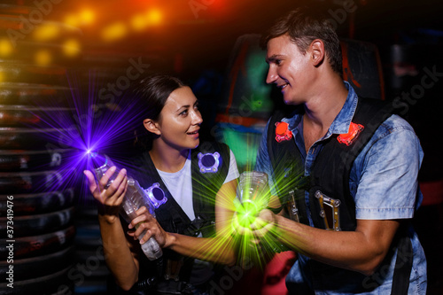 happy young couple holding colored laser guns during laser tag game in labyrinth