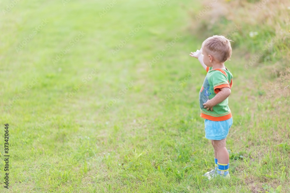 Boy shows his finger the direction while standing on a green lawn Boy shows his finger the direction while standing on a green lawn