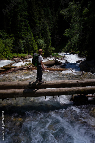 Hiker man hiking crossing river walking in balance on fallen tree trunk