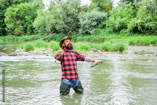 Fisher masculine hobby. Fisher fishing equipment. Fish on hook. Brutal man wear rubber boots stand in river water. Satisfied fisher. Fishing requires you to be mindful and fully present in moment