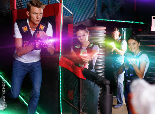Portrait of positive glad young friends standing with laser guns during laser tag game in dark room