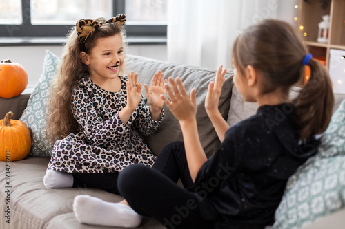 halloween, holiday and childhood concept - smiling little girls in party costumes playing clapping game at home