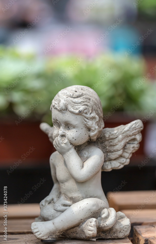 Winged little angel sculpture among flowers Winged little angel sculpture among flowers