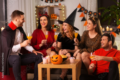 friendship, holiday and people concept - group of happy smiling friends in halloween costumes of vampire, devil, witch and cheetah with non-alcoholic drinks at home party at night