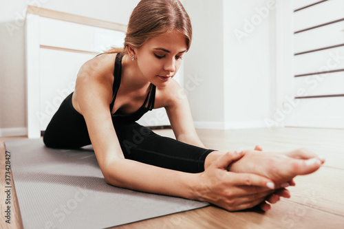 Focused blonde woman doing sports at home, doing leg stretching exercise