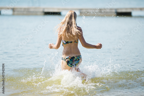Young blonde woman running to swim in water in sunny day. Back view. Enjoying summer holidays.
