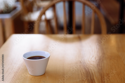 White cup with freshly brewed aromatic coffee on a wooden table.