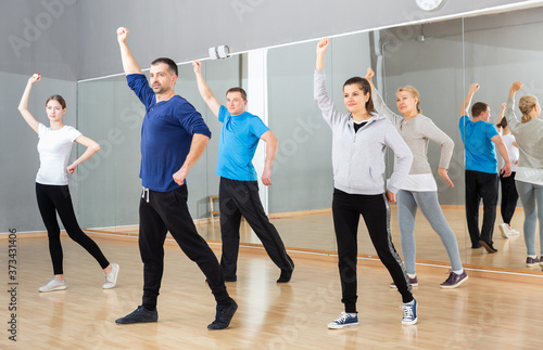 Group of sporty people doing stretching exercises before dance training in modern studio