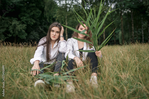 Two young caucasian girls posing sitting in the grass. The concept of friendship