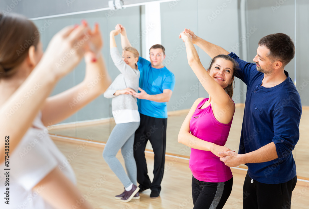 Group of happy adult people dancing modern social dances in pair at .dance school