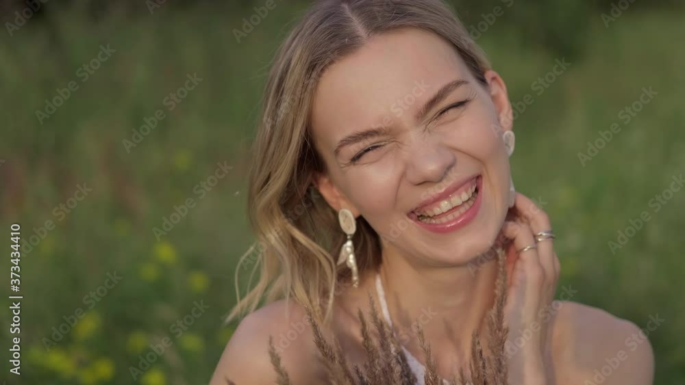 Portrait of young woman looking at camera and smiling. Happy woman enjoying nature at sunset. Summer day. 4K, UHD Portrait of young woman looking at camera and smiling. Happy woman enjoying nature at sunset. Summer day. 4K, UHD