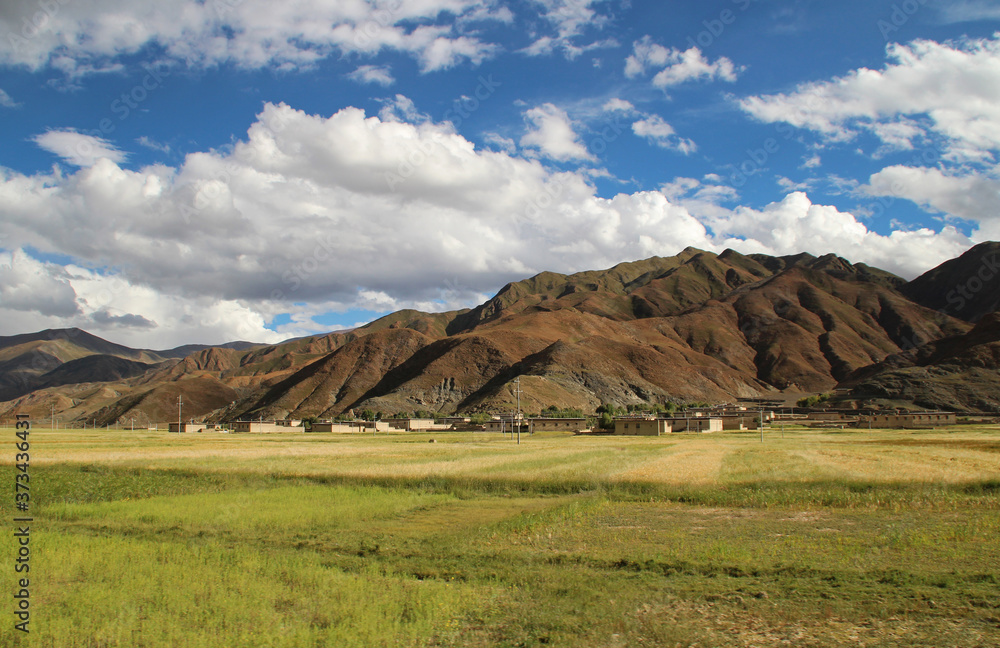 View of the mountains, barley field and Tibetan village with dramatic sky in Tibet, China 