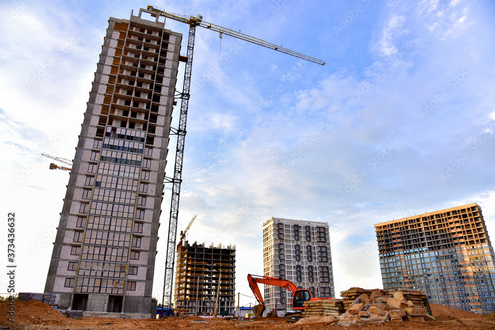 Fototapeta premium Large construction site with tower cranes and buildings on sunset background. Excavator during excavation for laying of underground storm sewer pipes. Tall house renovation project.