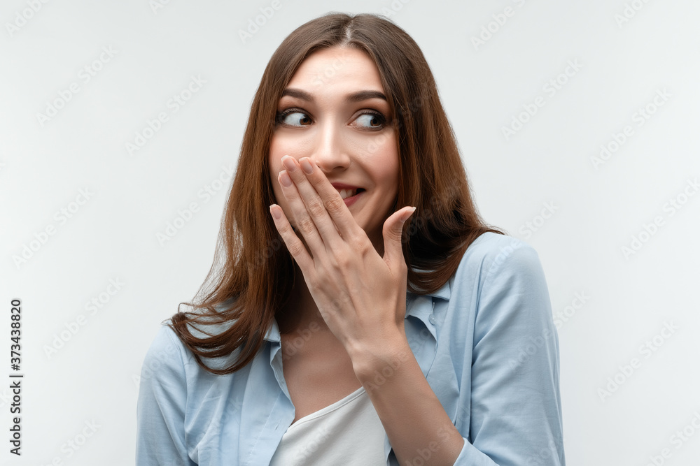 Charismatic girl with long chestnut hair covers her mouth with her hand. Human emotions, facial expression concept Charismatic girl with long chestnut hair covers her mouth with her hand. Human emotions, facial expression concept