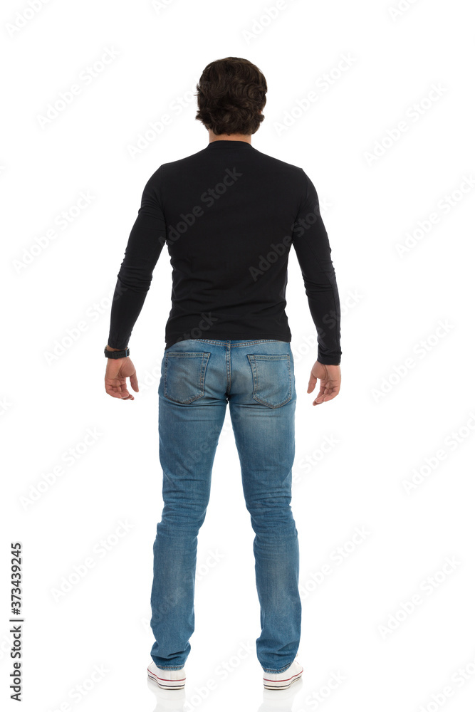 Standing Man In Sneakers, Jeans And Black Blouse. Rear View. Standing Man In Sneakers, Jeans And Black Blouse. Rear View.
