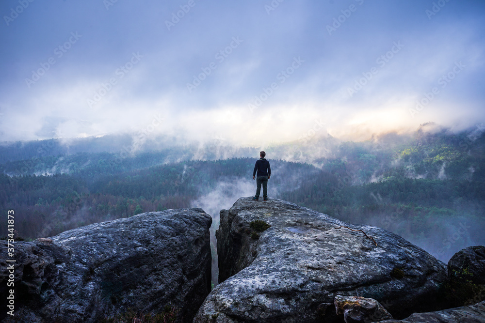 Hiker on top of a mountain looking into a valley with dramatic landscape in Saxon Switzerland, Germany