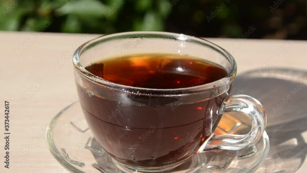 A girl pours tea from a transparent teapot into a transparent cup against a background of green foliage Good morning, outdoor cafe, energy boost. Tea being poured into glass tea A girl pours tea from a transparent teapot into a transparent cup against a background of green foliage Good morning, outdoor cafe, energy boost. Tea being poured into glass tea