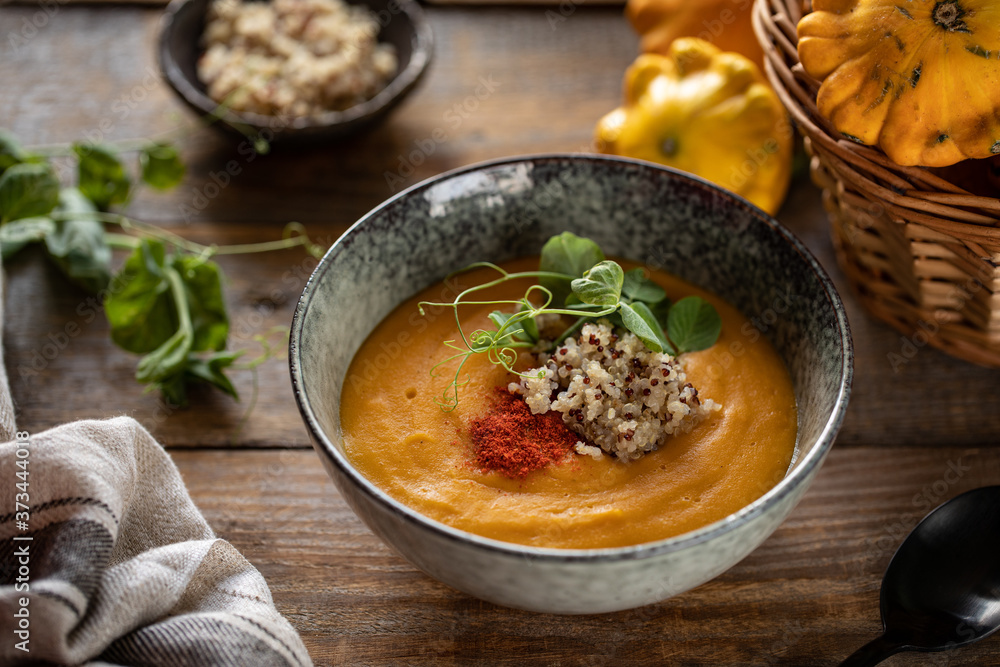Pumpkin cream soup with quinoa and sprouts of green peas in a dark plate on a dark wooden background Pumpkin cream soup with quinoa and sprouts of green peas in a dark plate on a dark wooden background