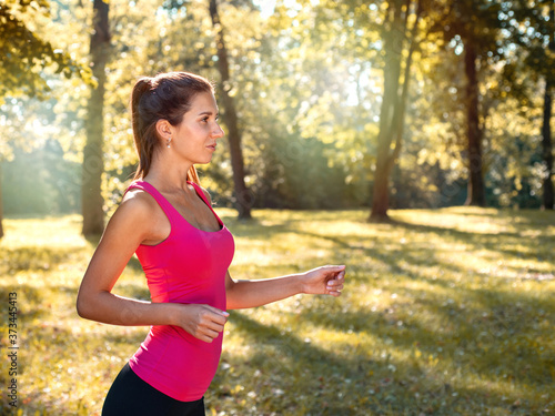 Portrait of young sporty brunette woman running in the park outdoor