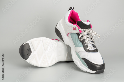 Weisse Damen-Sneaker mit hellblauen und rosaroten Akzenten. Mit grauem Hintergrund.