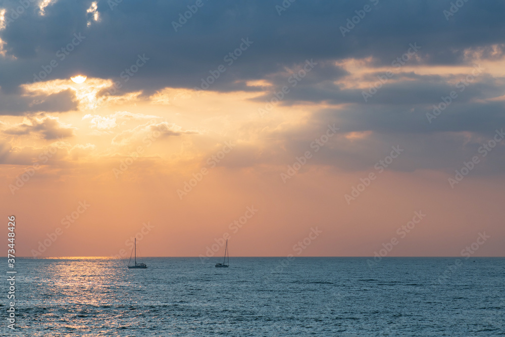 Seascape at sunset of the day. Calm. Sunset at sea. Sky with dark clouds in the sun Sailboats in the sea at sunset
