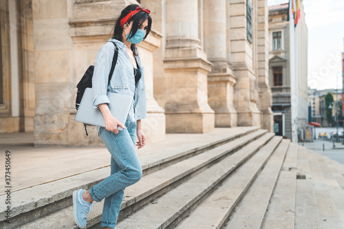 Girl student wearing protective face mask walking down university stairs during pandemic