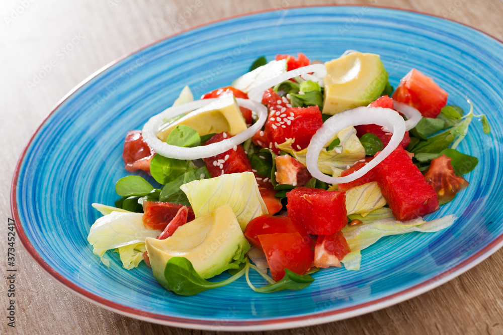 Vitamin salad from ripe watermelon, tomatoes, avocado, grapefruit and fresh cornsalad in blue plate