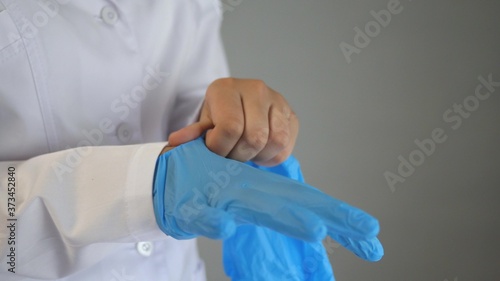 A doctor in a dressing gown puts on his hands blue sterile gloves made of natural latex. Health, medicine and pandemic concept. Covid-19. Close-up.