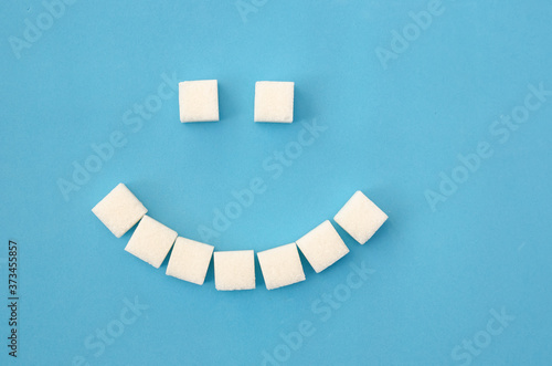 White sugar cubes laid out in the form of a smile on a blue background close-up. Concept of health, dentistry