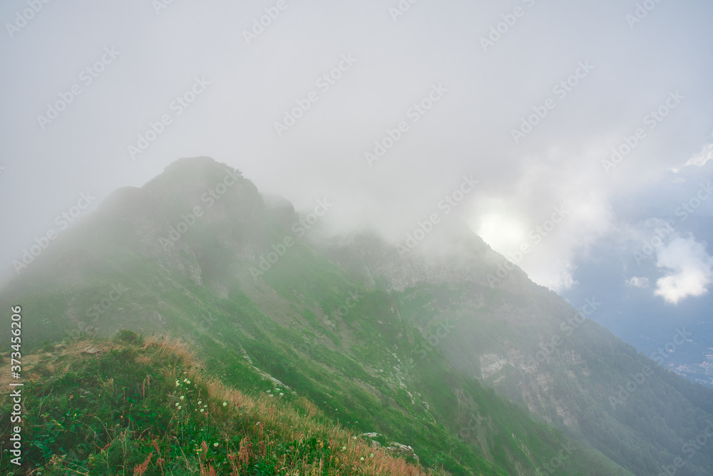 High-altitude landscape with mountain tops covered with clouds and green Alpine grass.