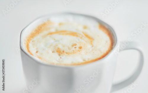 Light faceted cup with a delicate cappuccino with caramel and thick foam on a light background. An invigorating drink in the early morning.