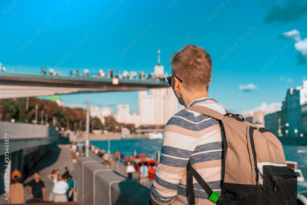Fototapeta premium A male tourist with a backpack sits on the embankment and admires the view of the floating bridge in Zaryadye Park, Moscow, Russia