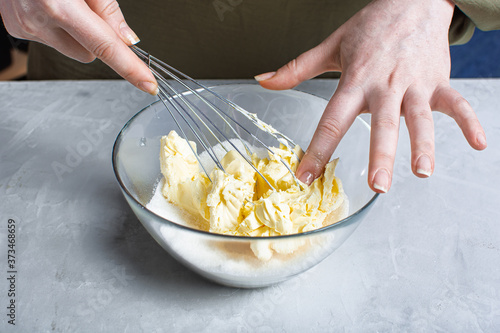 the chef's hands whisk butter and sugar in a glass bowl on a light stone table